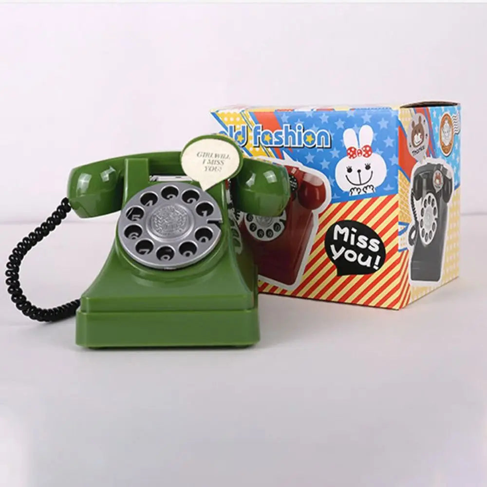 A vintage green rotary telephone piggy bank with a white button and a yellow and red box featuring a rabbit design.