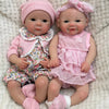 A realistic soft silicone reborn baby doll with a pink outfit and bonnet sitting on a light textured surface.