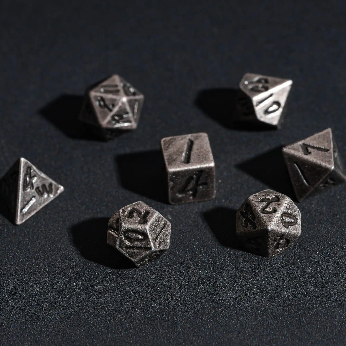 A collection of small, silver-colored metal dice scattered on a dark surface.