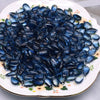 A pile of dark blue water drop Czech glass beads for jewelry making displayed on a white plate.