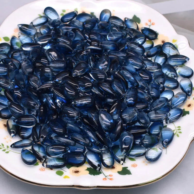 A pile of dark blue water drop Czech glass beads for jewelry making displayed on a white plate.