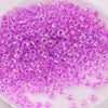 A pile of small, translucent purple glass rice beads for DIY jewelry and crafting.