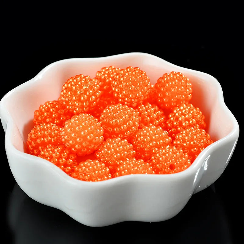 A white bowl filled with bright orange spherical pearl beads for jewelry making