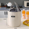 A white stackable bento lunch bag with a gray fabric lid is shown on a table.