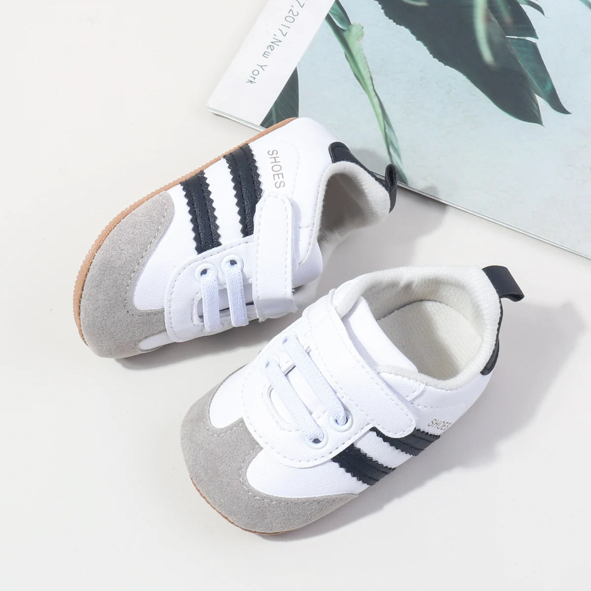 A pair of white and black striped baby first walkers soft sole shoes resting on a light surface.