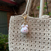 A light beige crocheted handbag with a gold-toned keychain featuring a small white rabbit charm.