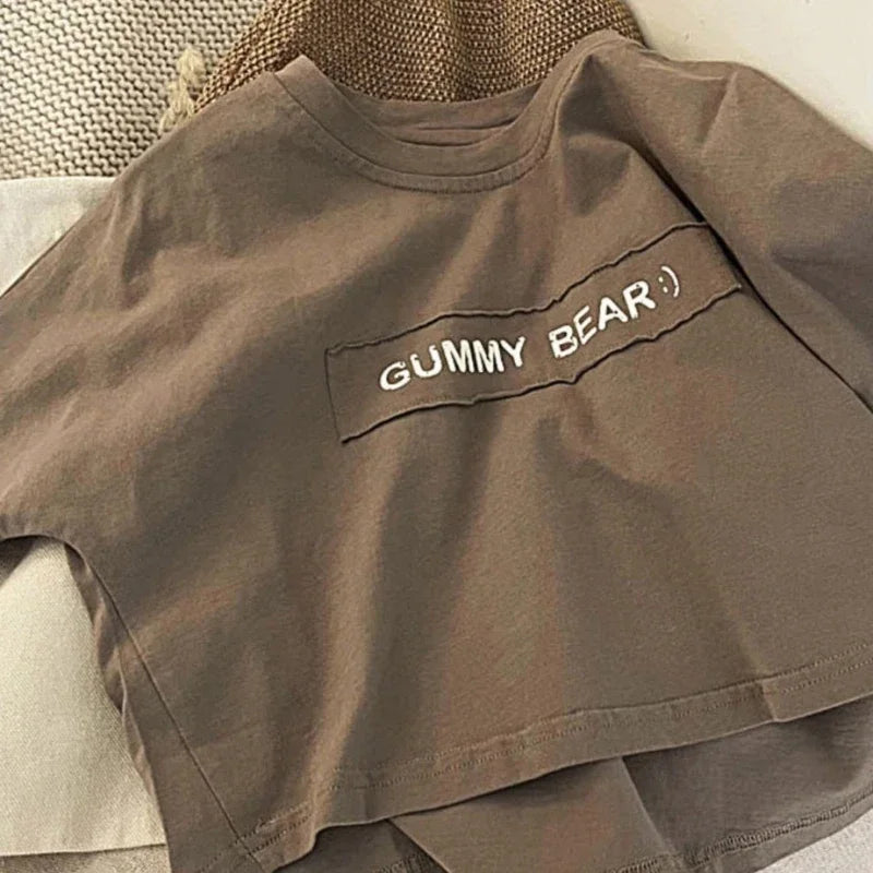 A plain taupe short-sleeve t-shirt with the text GUMMY BEAR printed on the chest.