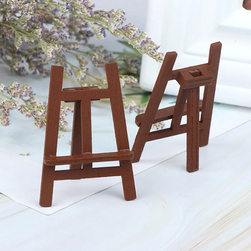 A miniature wooden artist easel for a dollhouse, made of brown wood, set against a white background with lavender flowers.