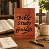 A leather-bound Bible study guide book resting on a wooden table next to a notebook and glasses.