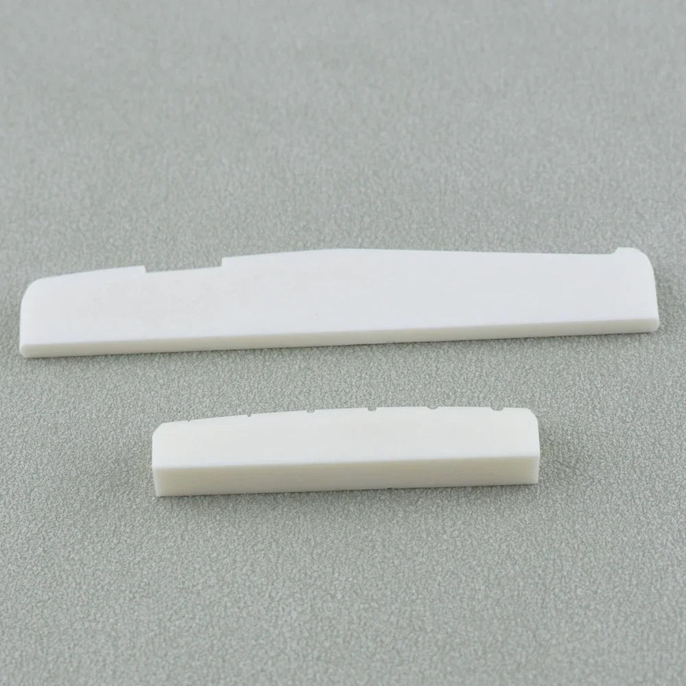 Two white guitar nut and bridge saddle components lying on a gray surface