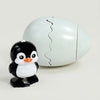 A white, egg-shaped toy with a cracked top and a small black and white penguin figure lying next to it.