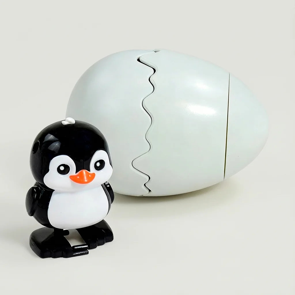 A white, egg-shaped toy with a cracked top and a small black and white penguin figure lying next to it.