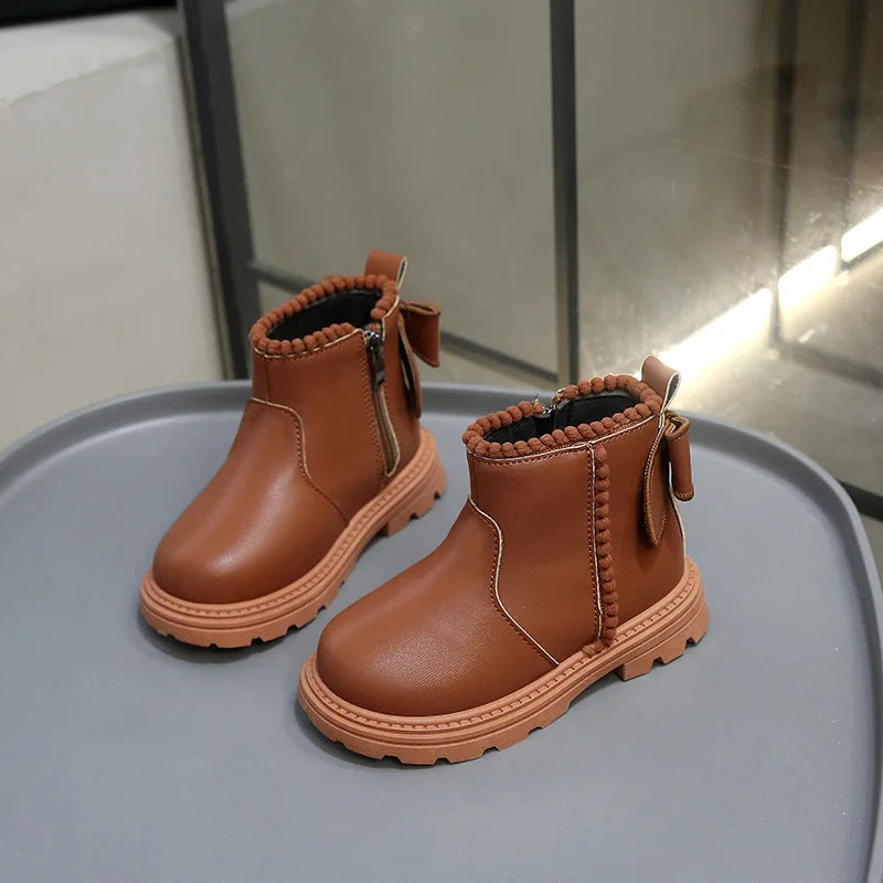 A pair of tan faux leather winter boots for kids, shown from the side on a gray surface.