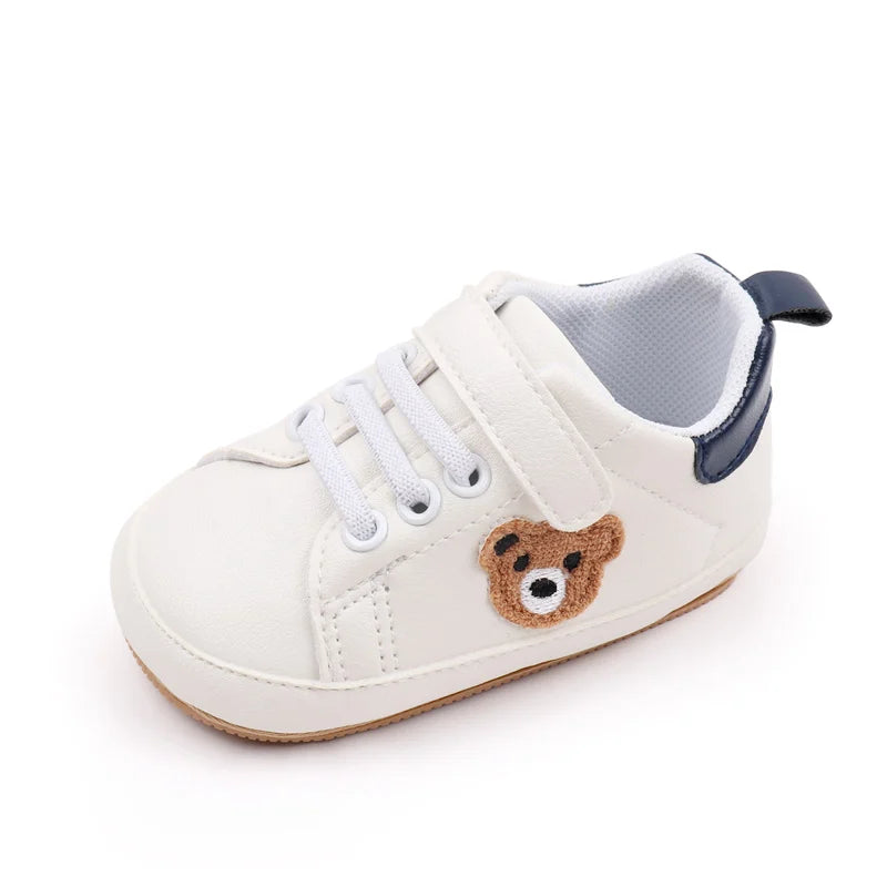 A pair of light beige baby sneakers featuring a cute brown bear design on the side.