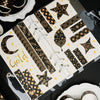 A set of black and gold foil washi tape rolls arranged on a clear sheet.