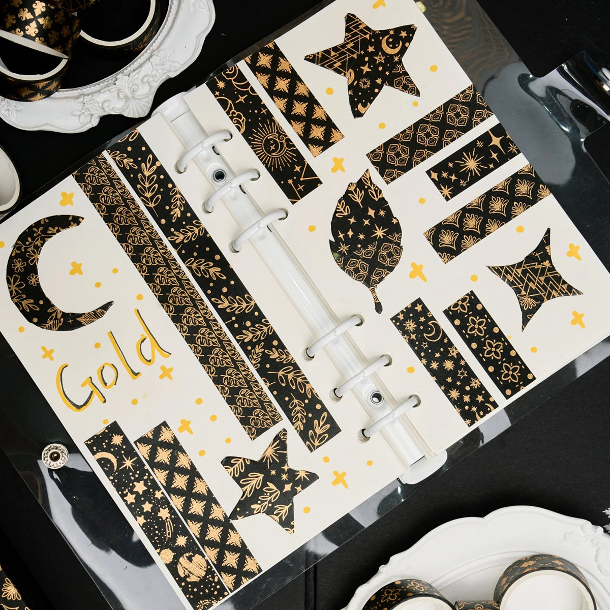 A set of black and gold foil washi tape rolls arranged on a clear sheet.