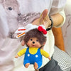 A small plush monkey charm pendant with brown fur, white ears, and a red bow is being held by a person.