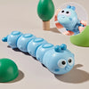 Blapesen-Wind-up-Spielzeug mit runden Augen und kleinen blauen Erhebungen neben einem grünen Gegenstand