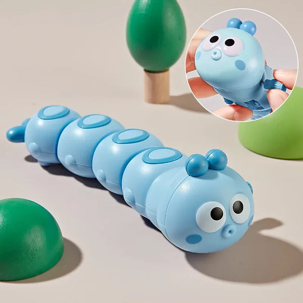 A blue cartoon caterpillar wind up toy with round eyes and small blue bumps is shown next to a green object.