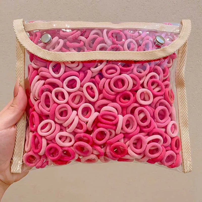 A pink multi-pack of colorful nylon elastic hair ties in various shades are displayed in a clear plastic bag.