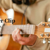 A hand is using a clip-on tuner on a wooden stringed instrument, likely a guitar or bass.
