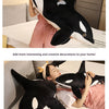 A woman is holding a large black and white orca whale plush toy in a bedroom setting.