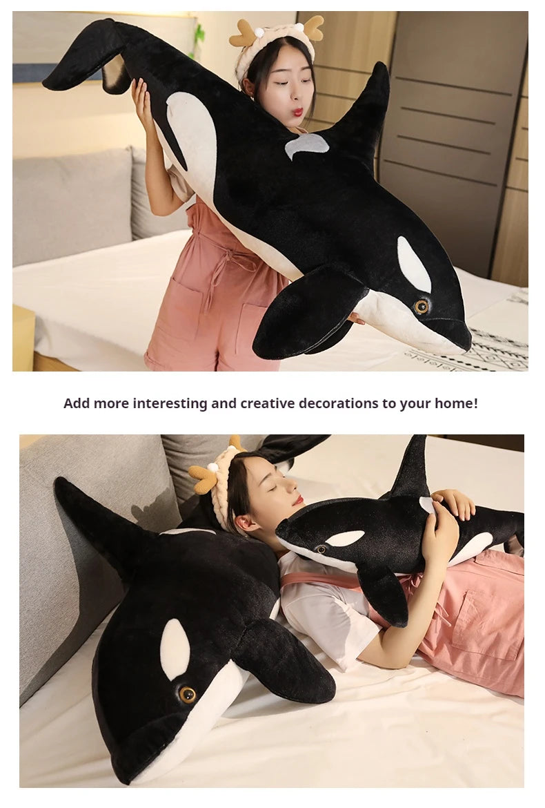 A woman is holding a large black and white orca whale plush toy in a bedroom setting.