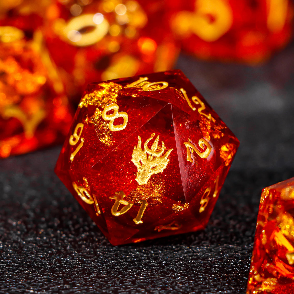 A close-up of a translucent red resin die with gold markings, resting on a dark surface.