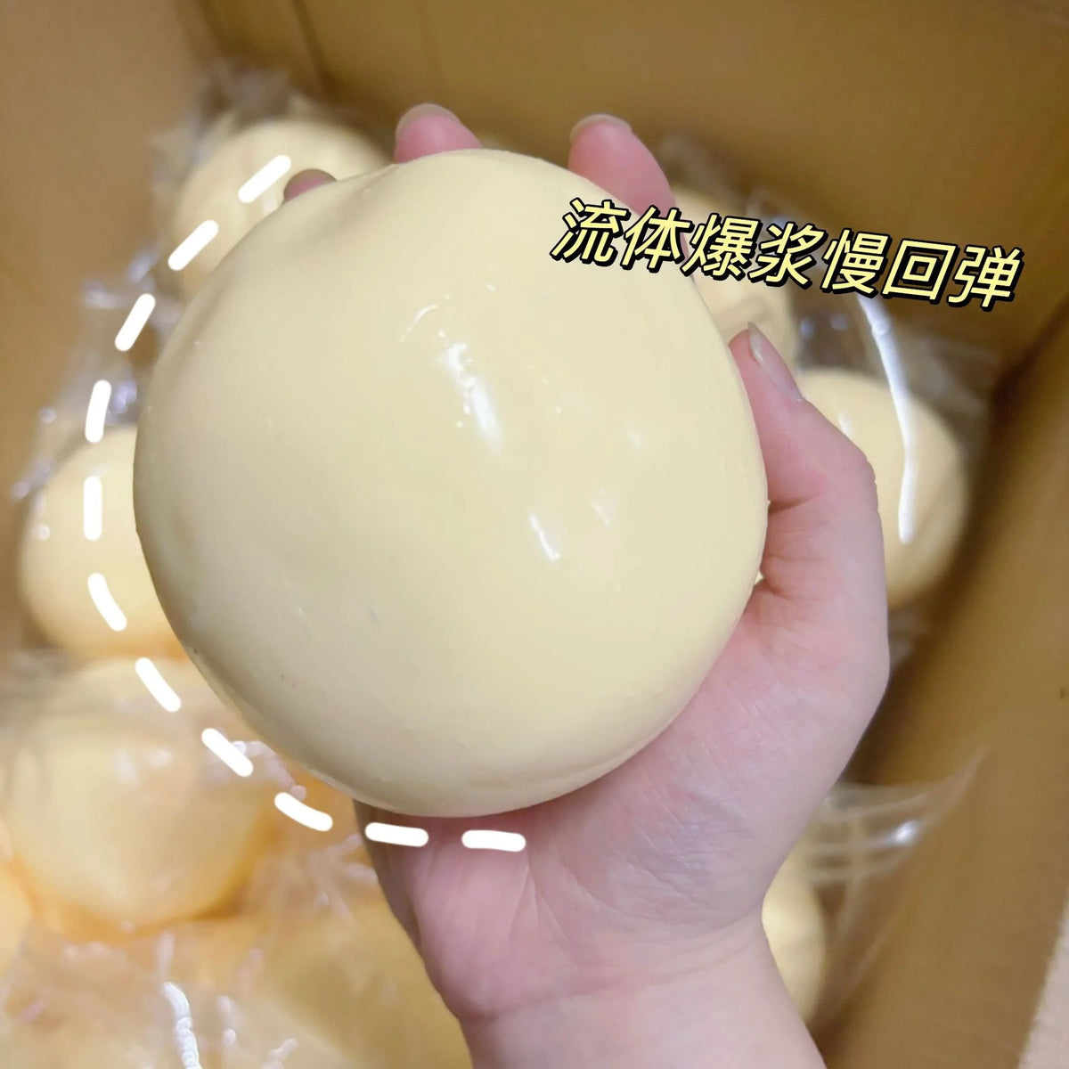 Eine Hand hält einen großen, glatten, hellgelben Stressball-Fidget-Spielzeug in einer Pappschachtel.