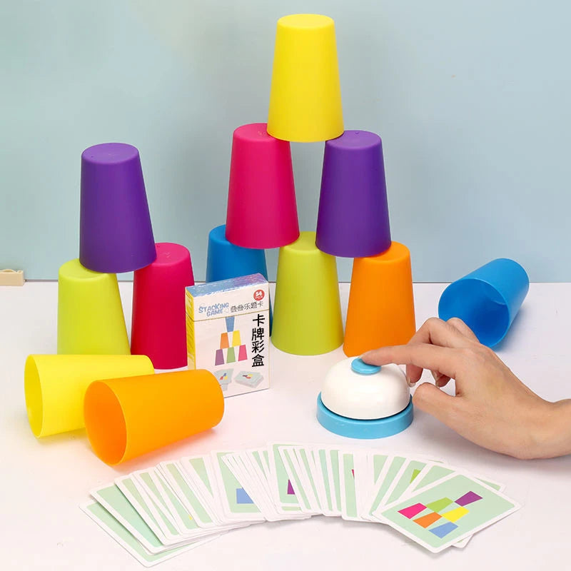 A set of colorful stacking cups and a bell toy are displayed on a white surface with several cards.