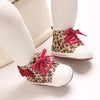 A pair of leopard print soft sole baby sneakers with white socks shown on a light background.