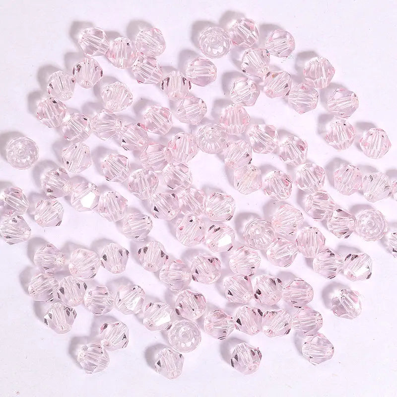 A pile of small, faceted pink crystal bicone glass beads for jewelry making.