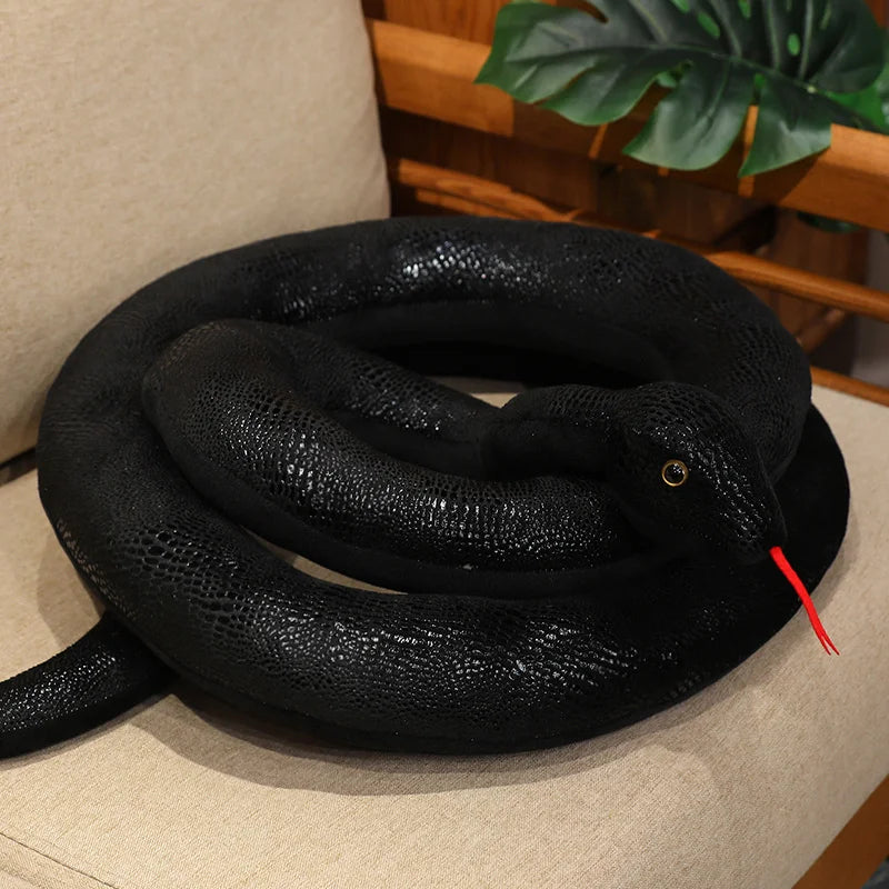 A realistic black giant snake plush toy is coiled on a light-colored surface.