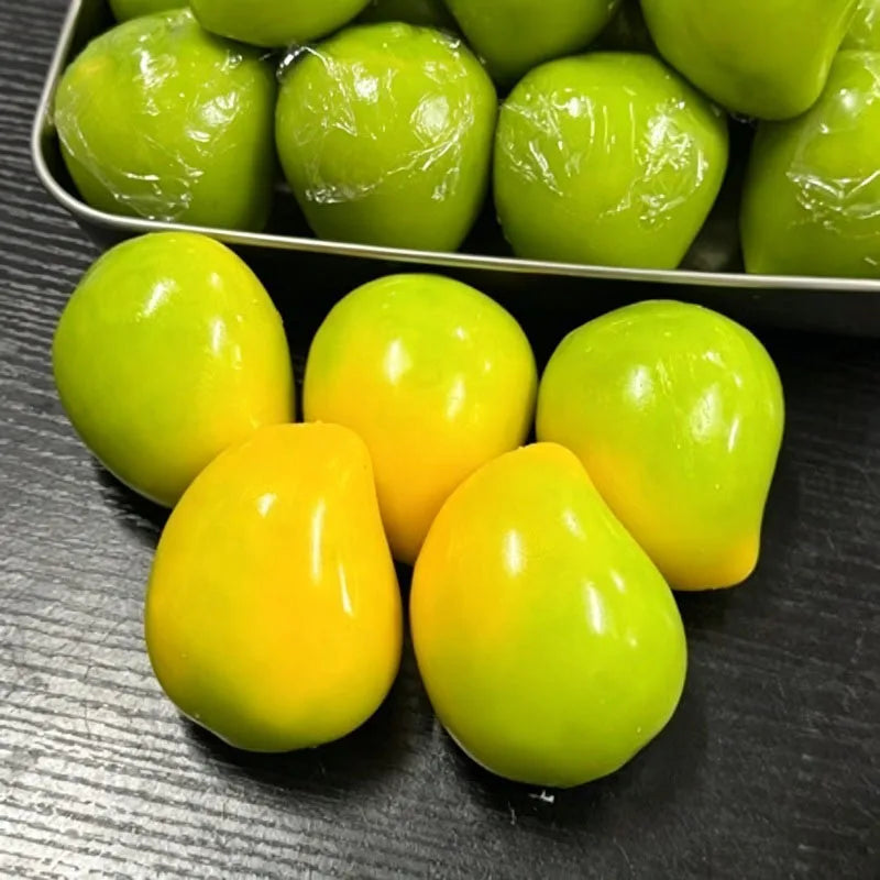 Eine Sammlung von leuchtend grünen und gelben Mango-förmigen Stressbällen in einer Metallschale.