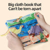 A hand holds a large cloth book featuring dinosaurs, demonstrating that the book cannot be torn apart.