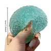 A hand holds a translucent aqua blue squishy ice ball fidget toy, showing its size relative to a ruler.