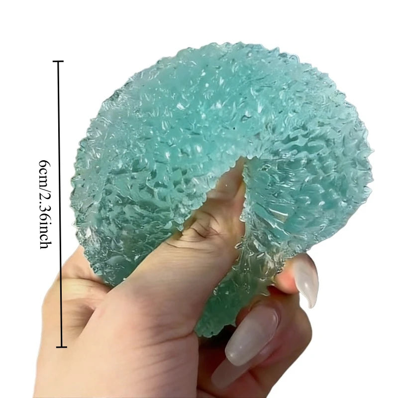 A hand holds a translucent aqua blue squishy ice ball fidget toy, showing its size relative to a ruler.