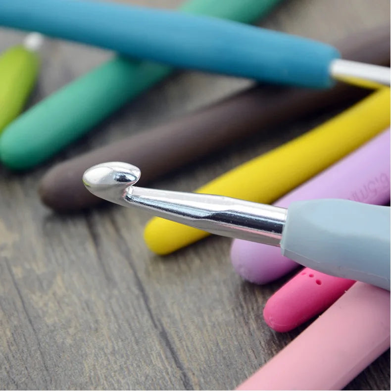 A collection of colorful ergonomic crochet hooks, stitch markers, and needles laid on a wooden surface.