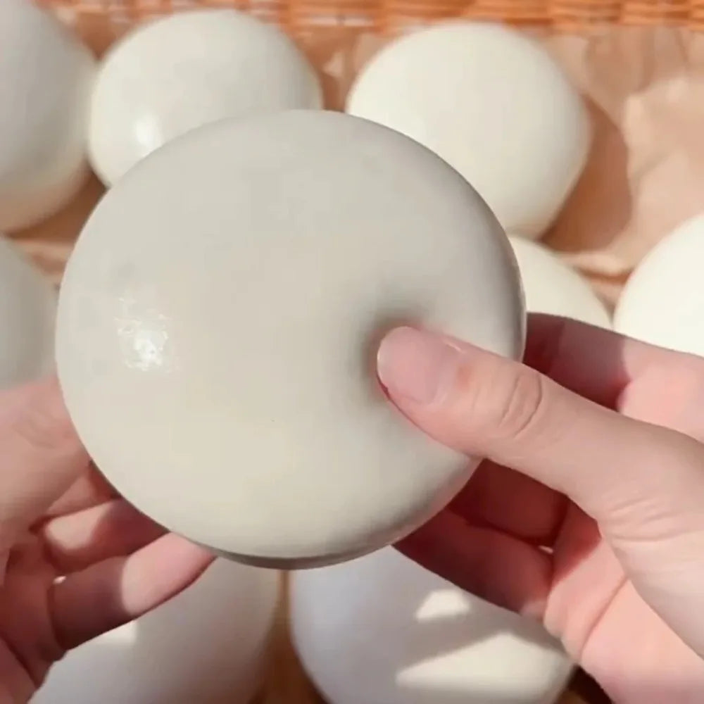 A hand is squeezing a smooth, white yogurt cake squishy stress relief toy against a background of similar items.