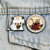 A silver enamel pin featuring a cute bear character and text on a denim jacket fabric.