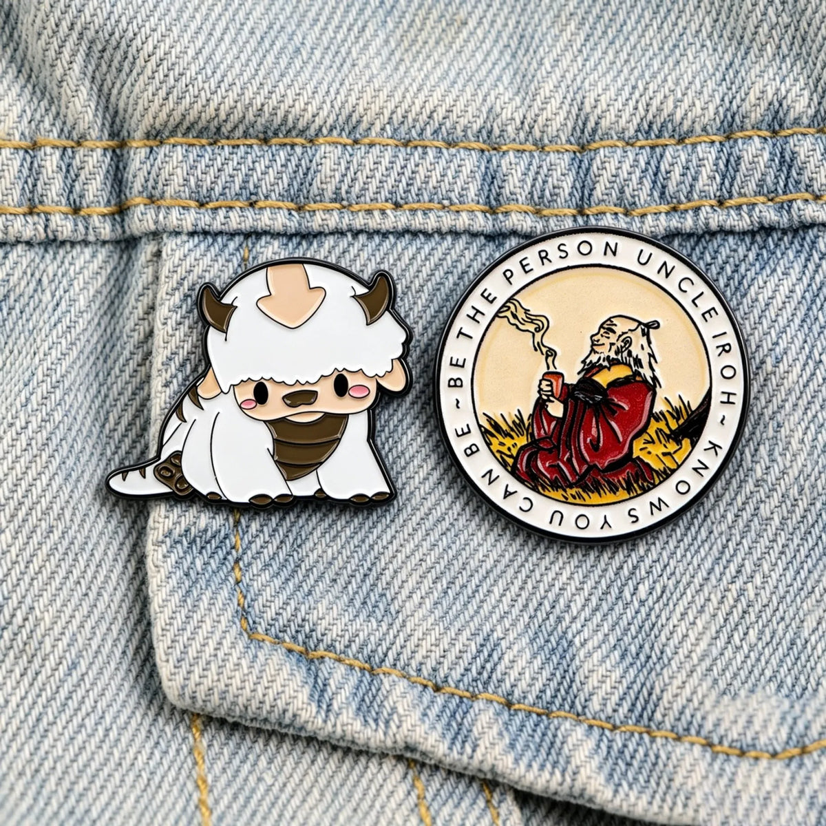 A silver enamel pin featuring a cute bear character and text on a denim jacket fabric.