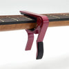 A close-up of a red aluminum alloy quick-change guitar capo mechanism attached to a wooden guitar neck.