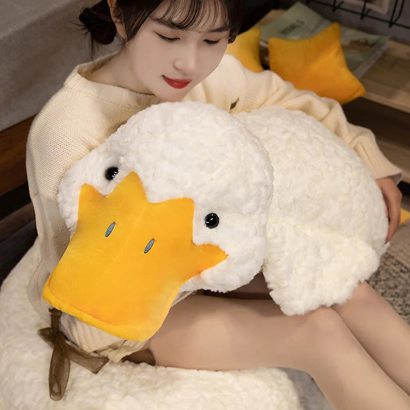 A woman is cuddling a giant white plush duck pillow with an orange beak and yellow accents.