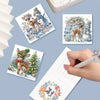 A hand is writing on a greeting card featuring deer and snow scenes, with several related cards displayed.