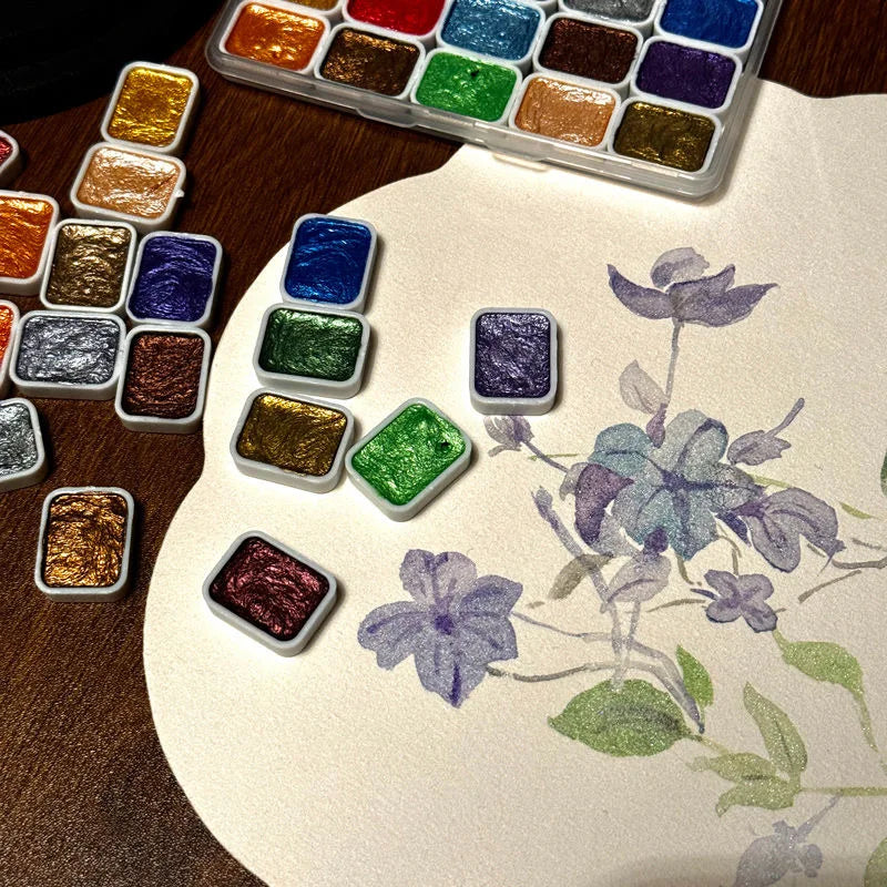 A collection of 20 metal watercolor paint colors arranged in a plastic palette on a light surface.