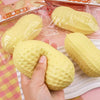 A hand is squeezing a yellow strawberry-shaped fidget toy packaged in plastic.