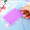 A hand is using a tool to paint on a purple diamond painting canvas inside a clear storage tray.