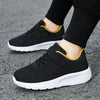A pair of black mesh sneakers with yellow accents and white soles worn by a person.