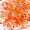 A pile of faceted crystal bicone glass beads in shades of orange and amber for jewelry making.