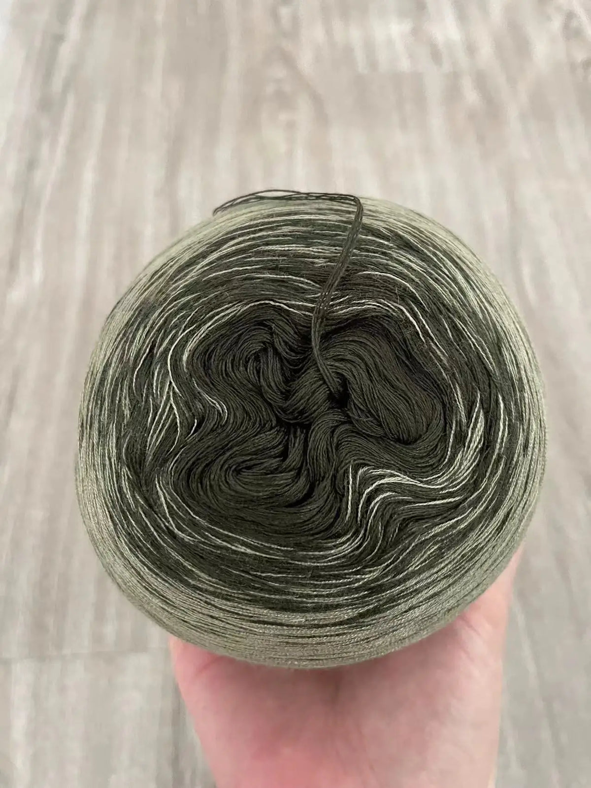 A ball of gray and white rainbow gradient mercerized cotton cake yarn is held in a hand.